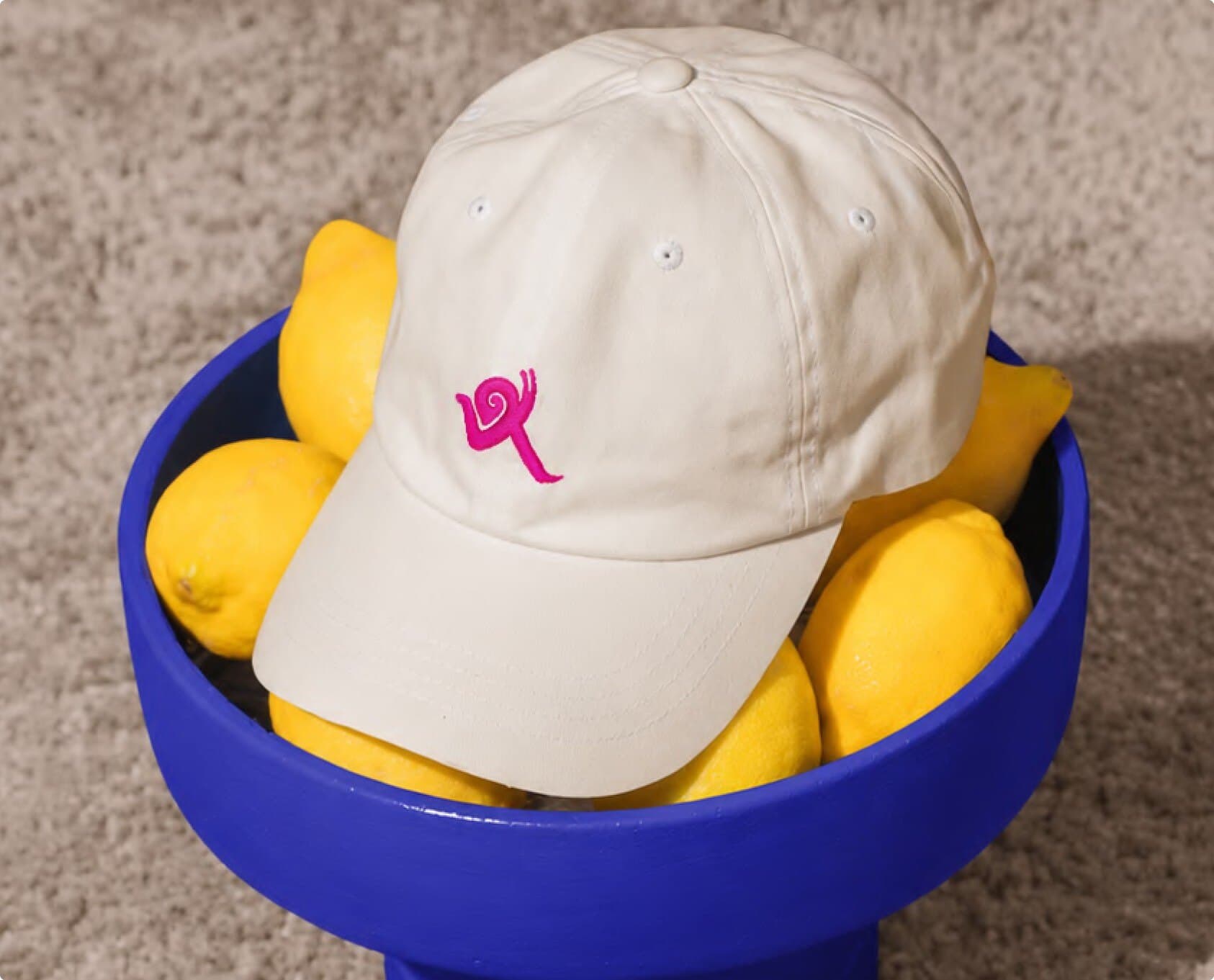 Cream cap with the pink sprinting-figure icon in a blue bowl of lemons